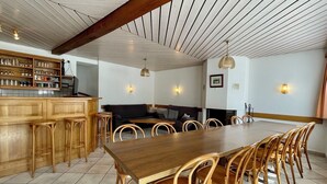 Un comedor con mesa y sillas de madera, una zona de bar con taburetes y una cocina con estantes.