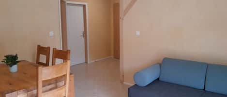 Una habitación con una mesa de comedor de madera, sillas, un sofá azul y una puerta que da a otra habitación.