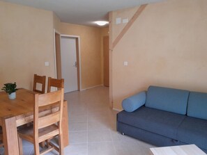 Ein Zimmer mit einem Holzesstisch, Stühlen, einem blauen Sofa und einer Tür zu einem anderen Raum.