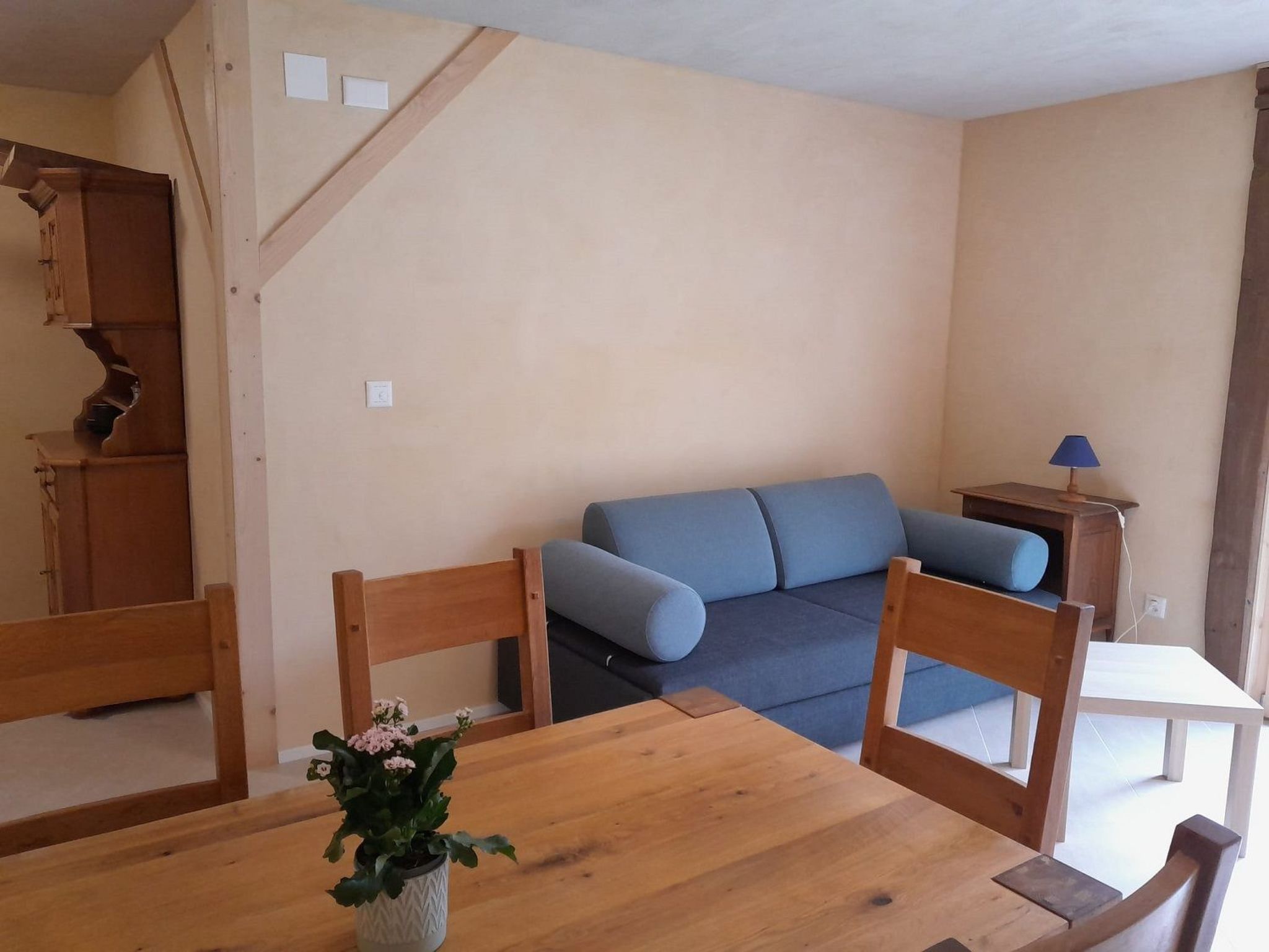 Une pièce comprenant une table à manger en bois, un canapé bleu et un petit meuble en bois.