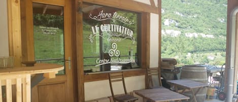 A wooden outdoor seating area with tables and chairs, a window with a view of greenery, and a sign indicating a natural center.