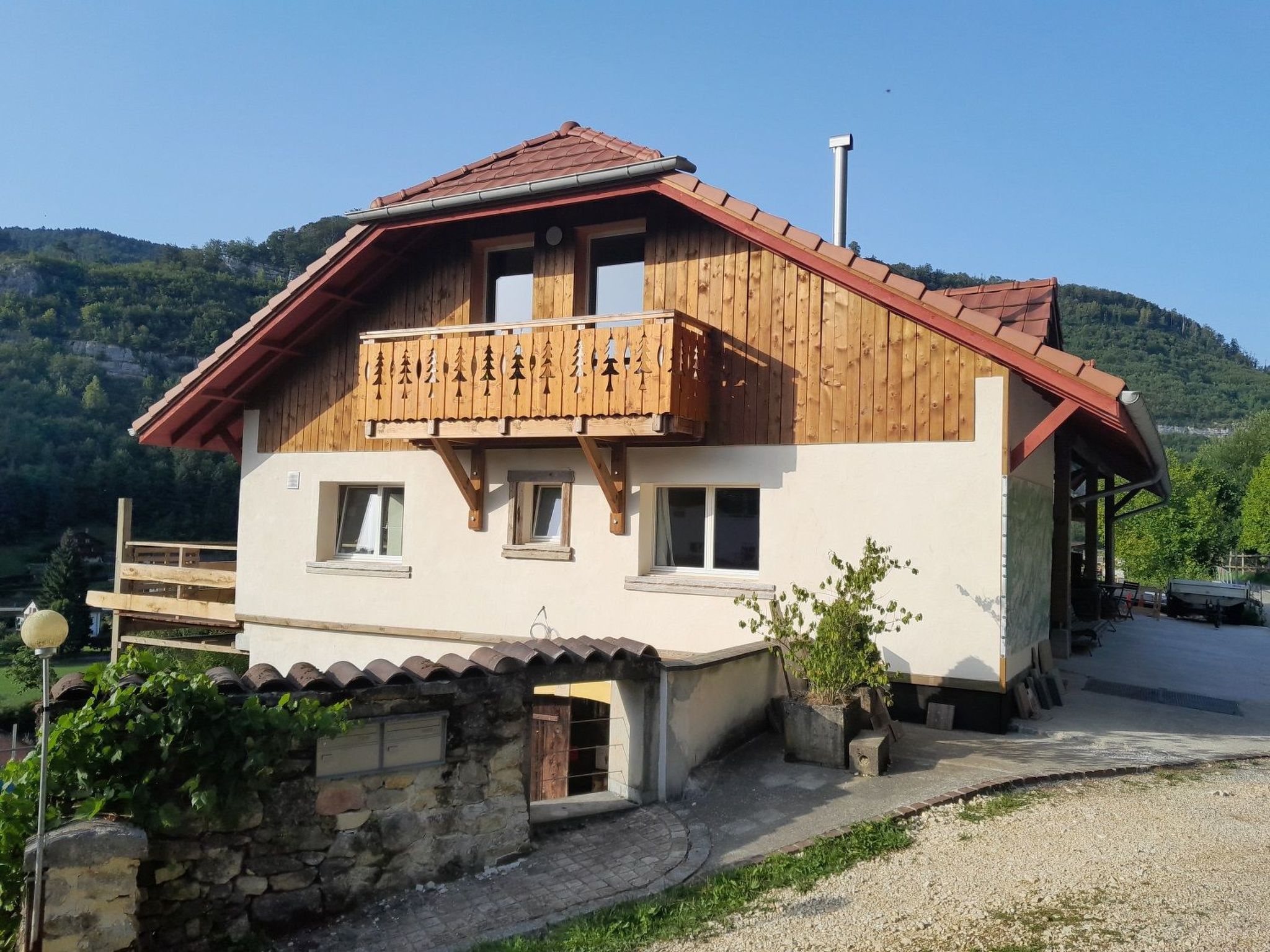 A two-story wooden chalet with a balcony, set against a mountainous backdrop.