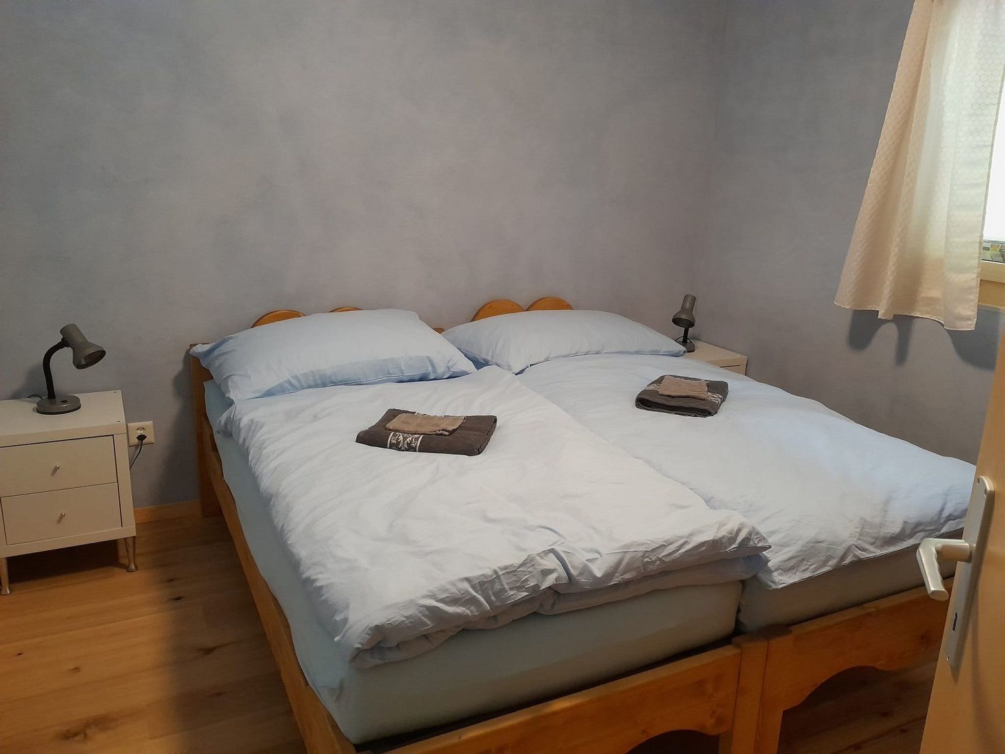 Un lit simple avec un cadre en bois, deux tables de chevet avec des lampes et une fenêtre avec un rideau.