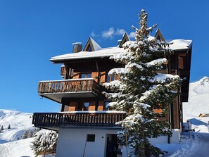 A multi-story wooden chalet with a balcony, surrounded by snow-covered trees and a clear blue sky. - Résid. Les Rhodos 3, (Les Crosets), by Interhome (Les Crosets)