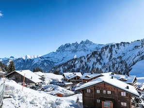 A snow-covered mountain village with wooden buildings and a clear view of the mountains in the background.