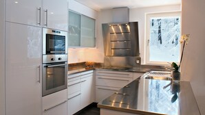 A modern kitchen with stainless steel appliances, white cabinetry, and a window with a view of a snowy landscape. - Chalet Altesse, (Zermatt), 1054.01 by Interhome (Zermatt)