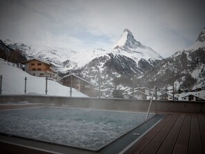 Un bain à remous sur une terrasse en bois, avec une montagne enneigée en toile de fond.