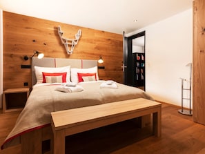 Une chambre moderne avec une tête de lit en bois, un lit avec une literie blanche et rouge, une table de chevet et un banc en bois.