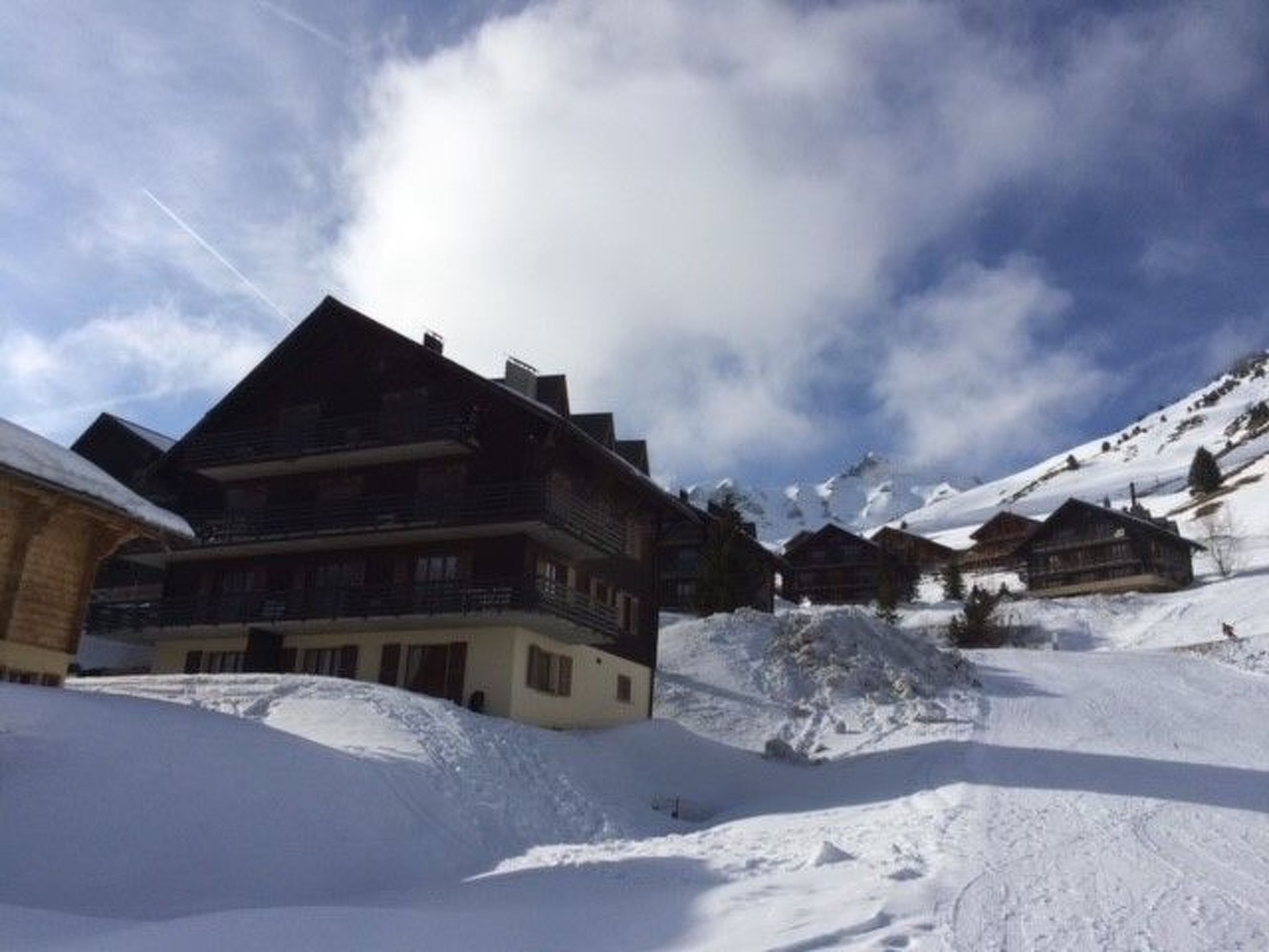 Un village de montagne enneigé, avec des maisons traditionnelles en bois et un grand bâtiment doté de nombreux balcons.