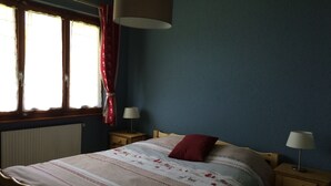 Ein Schlafzimmer mit einem Bett, zwei Nachttischen, einem Fenster mit Vorhängen, einem Heizkörper und einer Lampe auf jedem Tisch.