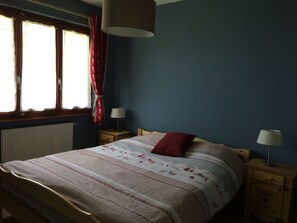 Un dormitori amb un llit, dues taules de nit, una finestra amb cortines i un radiador.