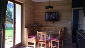 Ein Holzinnenraum mit Esstisch, Stühlen, Fernseher und Küchenzeile.