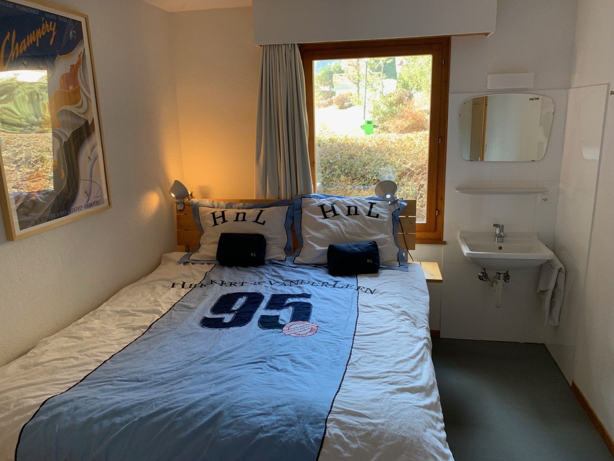 A bedroom with a bed, a window, a sink, and a mirror.