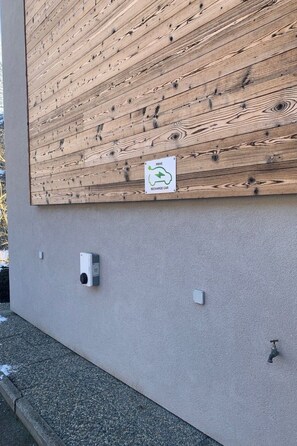 Ein Gebäudefassad mit Holzverkleidung, einem Schild für reservierte Ladestationen für Elektroautos und angebrachten Stromverteilern.