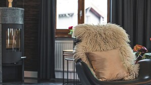 A modern living room with a black leather chair, a fluffy beige throw pillow, a fireplace, and a view of buildings through a window. - Haus Venus, (Zermatt), by Interhome (Zermatt)
