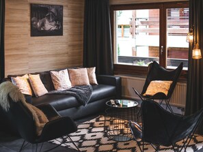 A modern living room with a black leather sofa, patterned cushions, a black armchair, a round coffee table, and a view of the outside through a large window. - Haus Venus, (Zermatt), by Interhome (Zermatt)