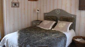 Ett sovrum med ett träpanelat tak, en säng med en fäll av fuskpäls, två hjärtformade kuddar, ett sängbord med en lampa och en liten korg.