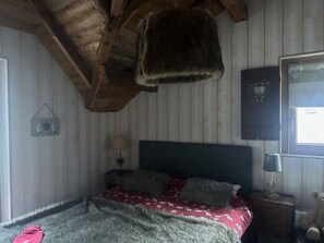 Ein Schlafzimmer mit Holzboden, einem Bett mit dunklem Kopfteil, einem Nachttisch mit Lampe und einer Wanddekoration.