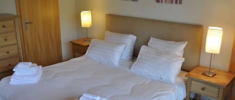 A neatly made bed with white linens and towels, two bedside tables with lamps, a wooden wardrobe, and a door.