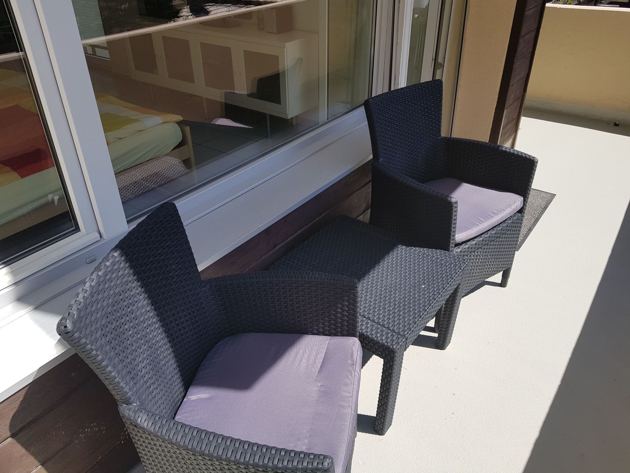 A patio area with two wicker chairs and a table, near a glass door.