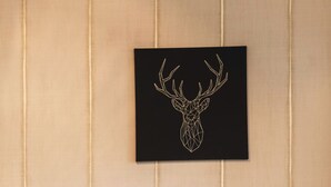 A room with a black sofa, patterned cushions, a knitted throw, and a framed deer head artwork on the wall. - Haus Venus, (Zermatt), by Interhome (Zermatt)