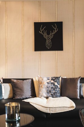 Ein Zimmer mit einer schwarzen Couch, gemusterten Kissen, einer Strickdecke und einem Bild einer Hirschkopf-Zeichnung an der Wand.