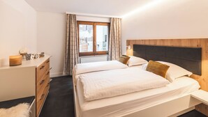 A hotel room with two beds, a dresser, a window with curtains, and a view of buildings outside. - Haus Venus, (Zermatt), by Interhome (Zermatt)