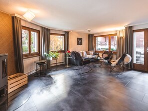 A modern living room with a fireplace, a sofa set, a dining table, and a view of the outside. - Haus Venus, (Zermatt), by Interhome (Zermatt)