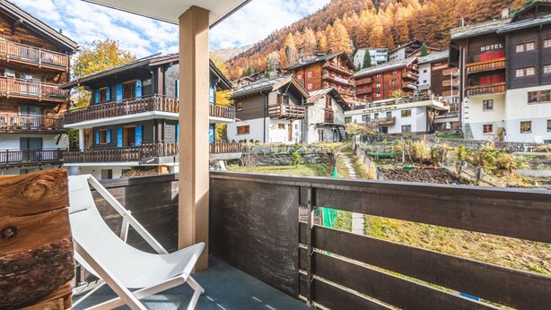 A balcony with a white chair, wooden buildings, and a mountainous backdrop. - Haus Venus, (Zermatt), by Interhome (Zermatt)
