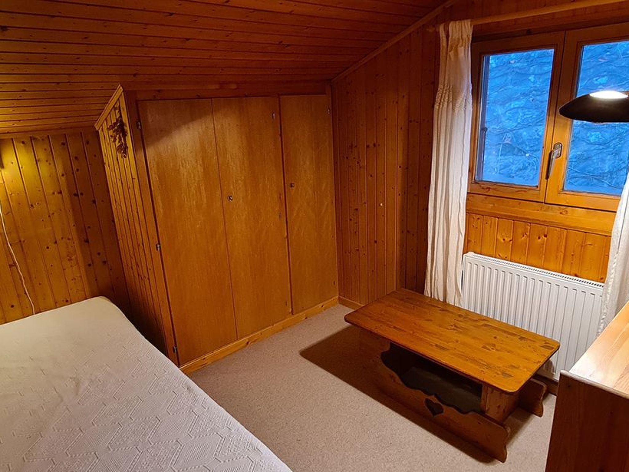 A wooden cabin room with a bed, a table, and a window with a view.