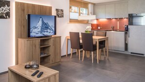 Una cucina moderna con forno a incasso e microonde, un'area pranzo con tavolo e sedie in legno, e un televisore montato su un mobile in legno.