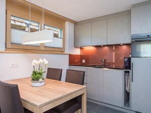 Une cuisine moderne avec un coin repas, comprenant une table en bois, des chaises, une plante en pot et un four encastré.