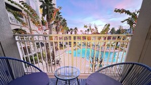 A balcony with two blue wicker chairs and a small glass table, overlooking a pool and palm trees. - 207 Luxury 2-Unit Suite Pool | Universal & I-Drive (Orlando)