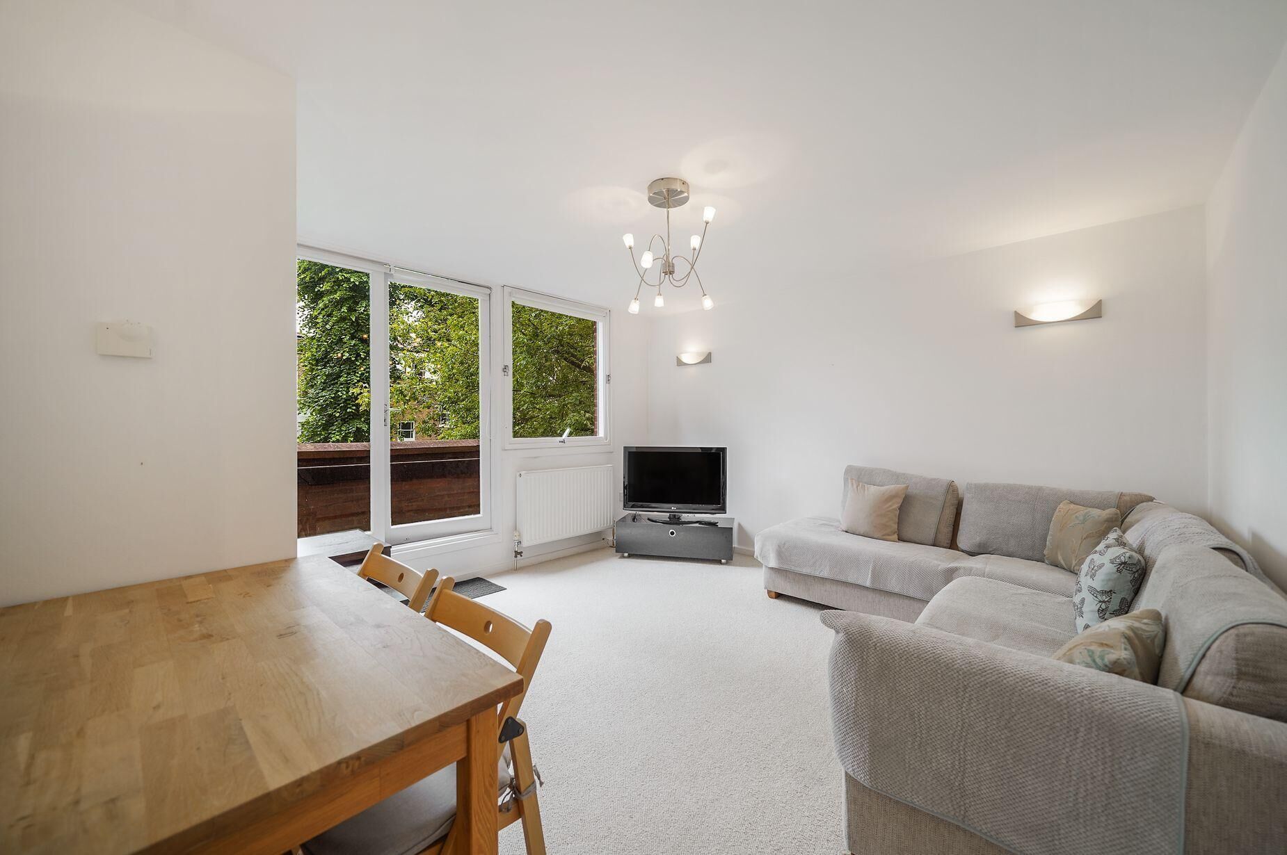 Ein Wohnzimmer mit Sofa, Fernseher, Esstisch, Stühlen und einem großen Fenster.