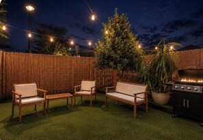 Eine Terrasse im Freien mit Holzmöbeln, Lichterketten, einem Grill und einem Holzzaun.