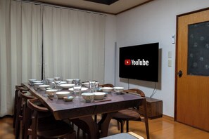 A dining area with a table set for four, a flat-screen TV mounted on the wall, and a wooden door. - White Dream Lodge Furano (Furano-shi /Kitanomine-cho)