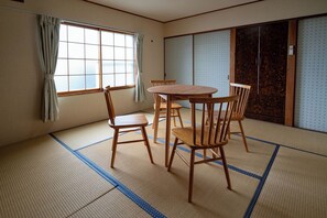 A tatami mat room with a wooden table and chairs, a sliding door, and a window with curtains. - White Dream Lodge Furano (Furano-shi /Kitanomine-cho)