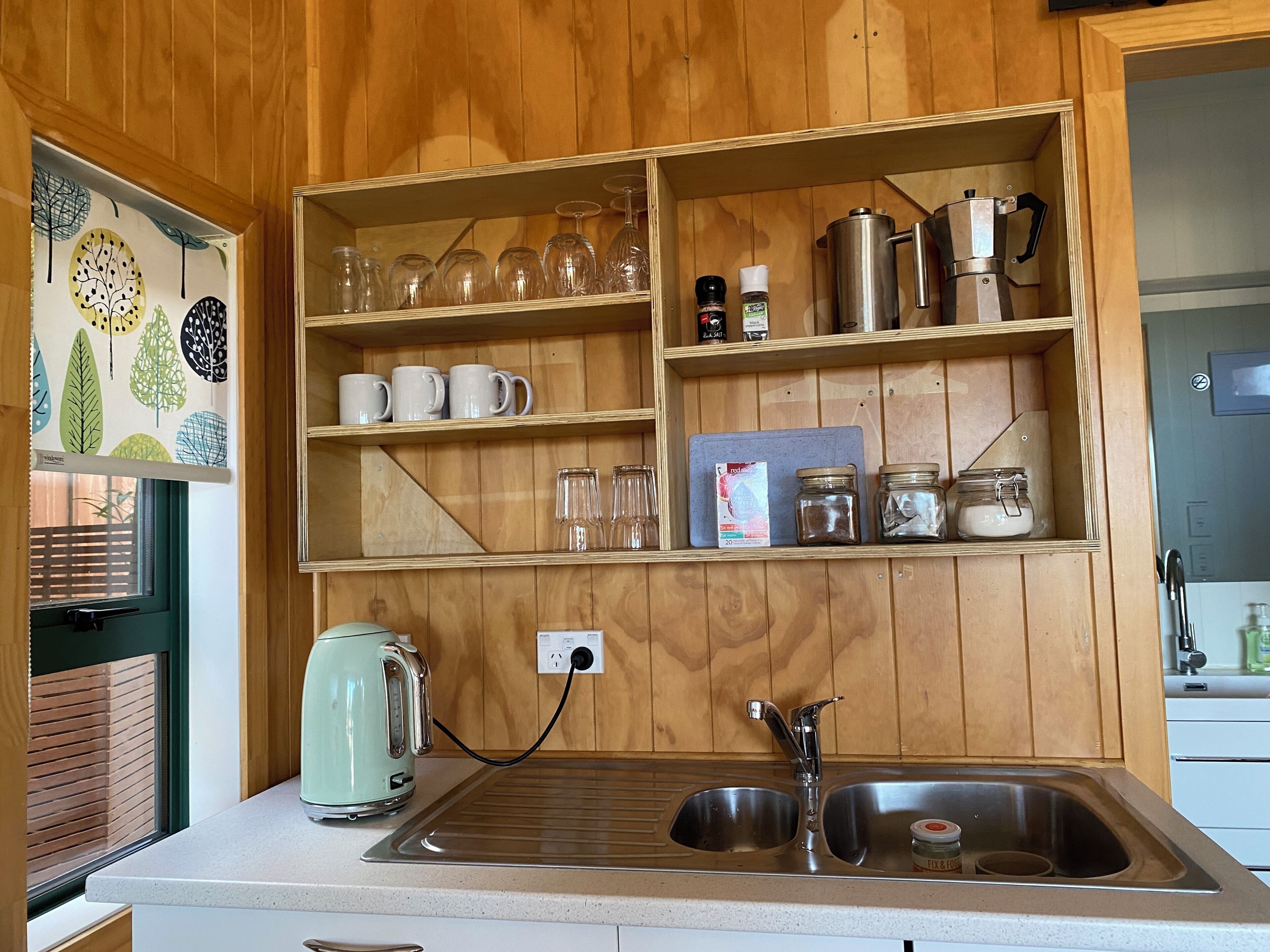 A kitchen with wooden cabinets, a kettle, a coffee maker, and a sink.
