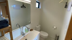 A compact bathroom with a white sink, a mirror, a toilet, and a small window.