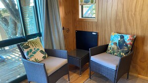 A room with wicker chairs, a small table, a window with curtains, and a door with a metal handle.