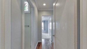Een gang met witte muren, houten vloer en een deur naar een andere kamer.