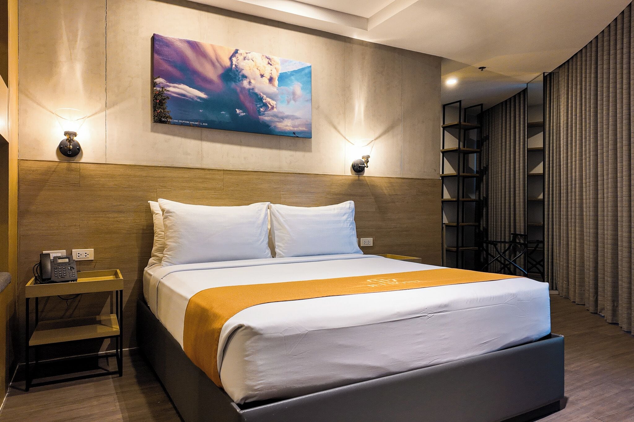 Ein Hotelzimmer mit Bett, Nachttisch, Lampe, Kunstwerken und Blick nach draußen.