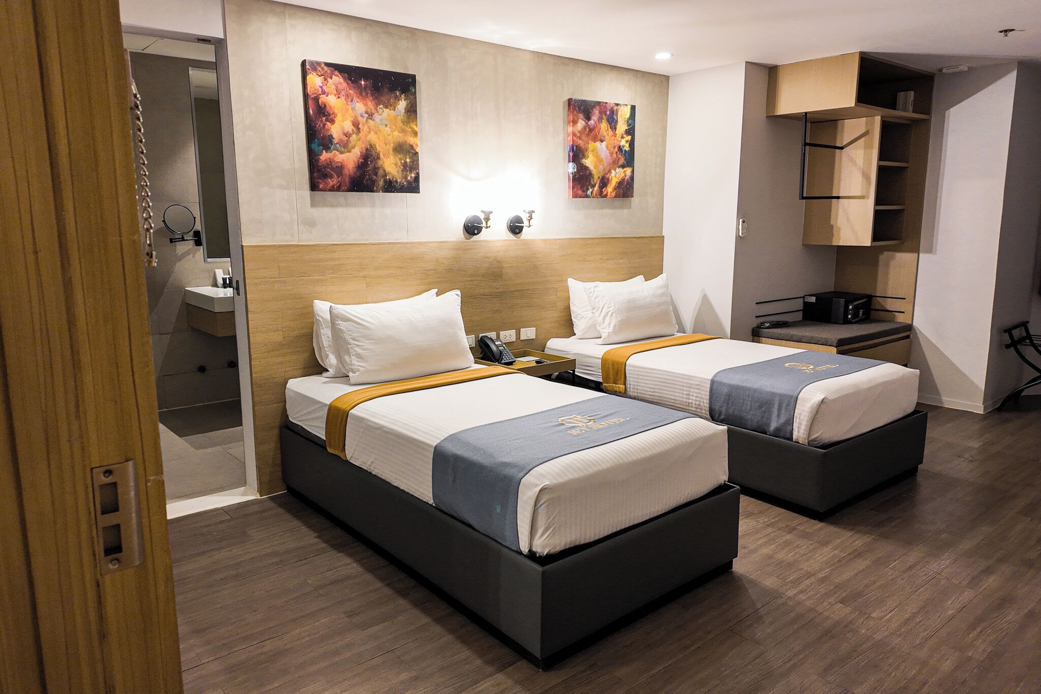 Habitación de hotel con dos camas, baño, escritorio y obras de arte en las paredes.