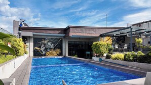 Una piscina con un mural, rodeada de follaje y un edificio moderno.
