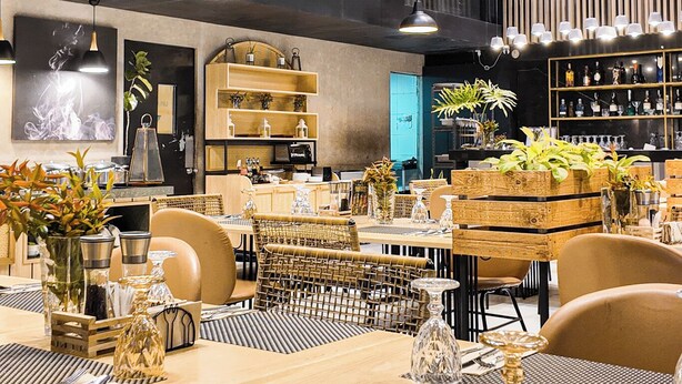 Un comedor moderno con techos altos, iluminación colgante y una combinación de mobiliario de madera y metal.