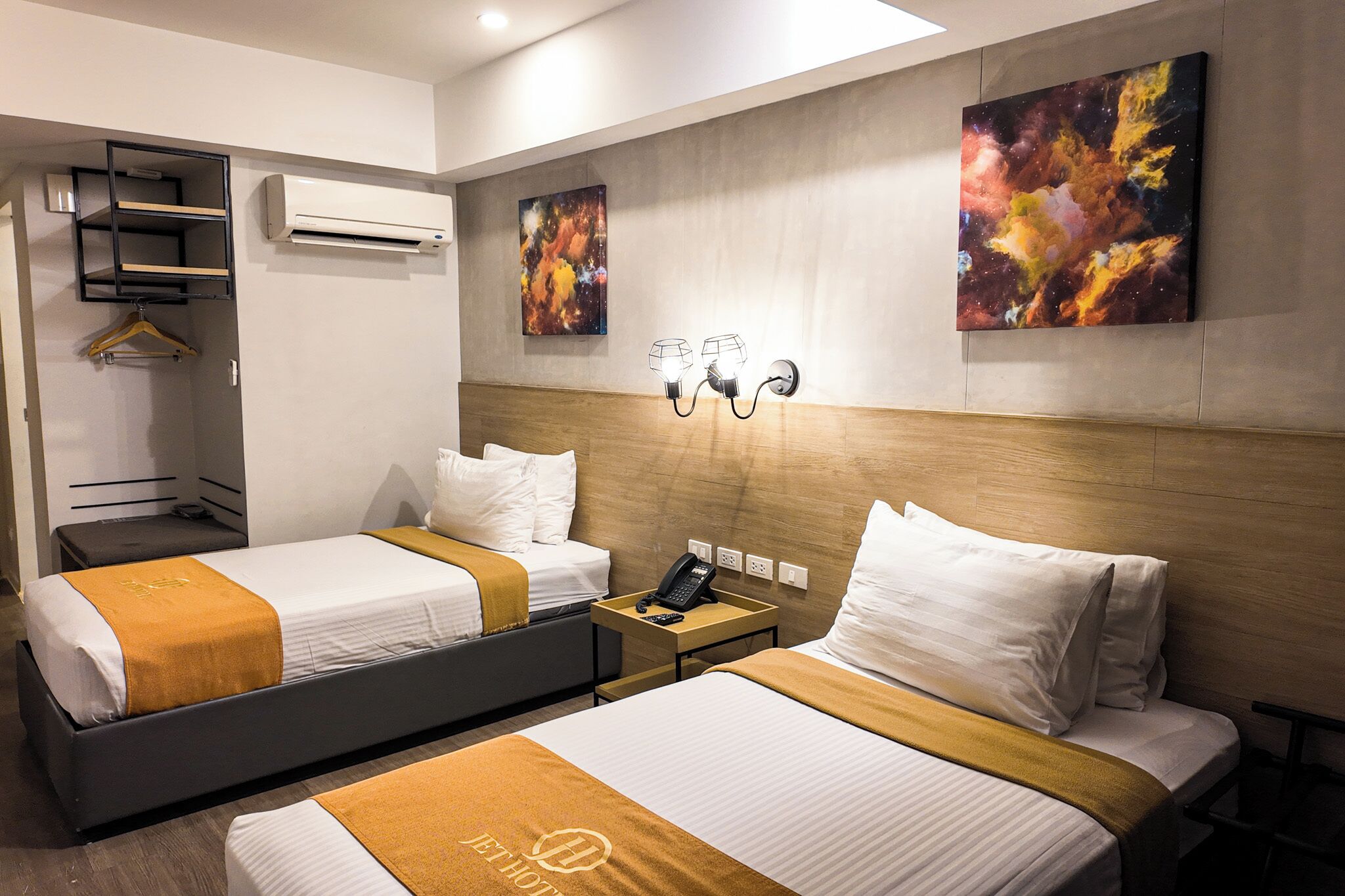 Habitación de hotel con dos camas, una mesita de noche con teléfono, obra de arte en la pared y unidad de aire acondicionado.