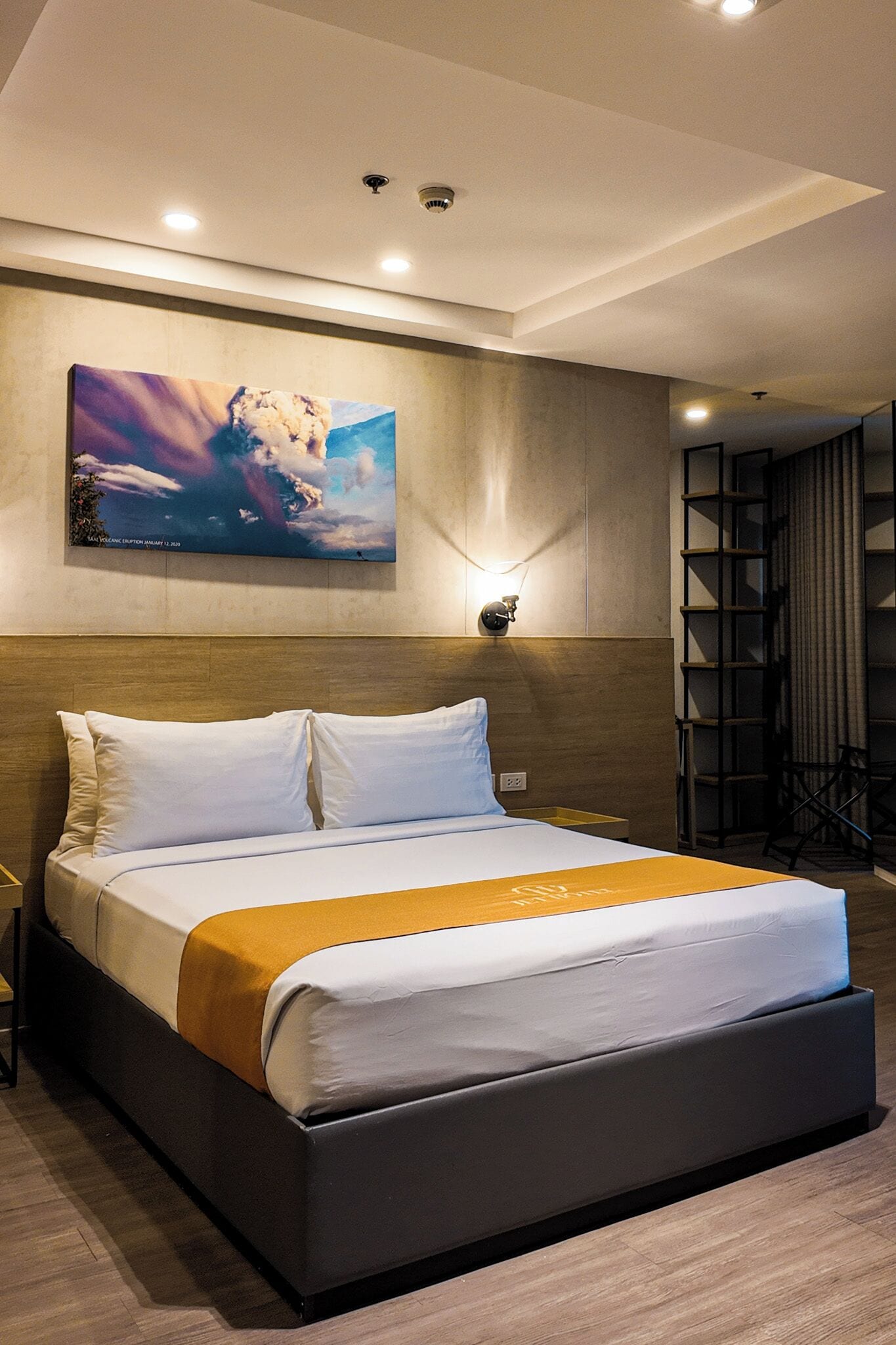 Una habitación de hotel moderna con una cama grande, un cuadro en la pared y una estantería.