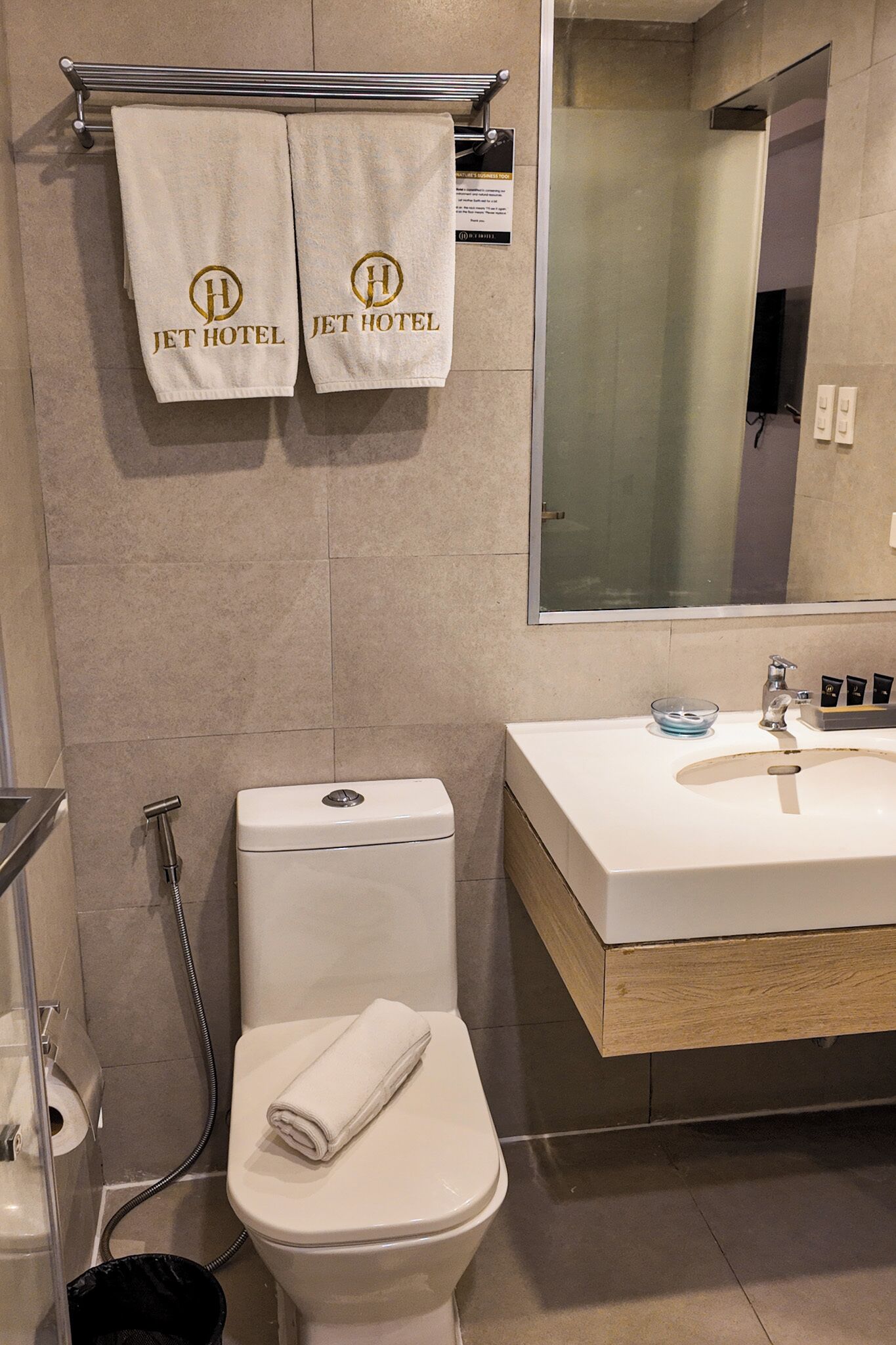 Un baño con inodoro, lavabo, ducha y dos toallas colgadas en un perchero.