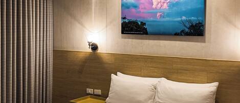 A hotel room with a bed, a nightstand, a painting of a sunset, and a ceiling light.