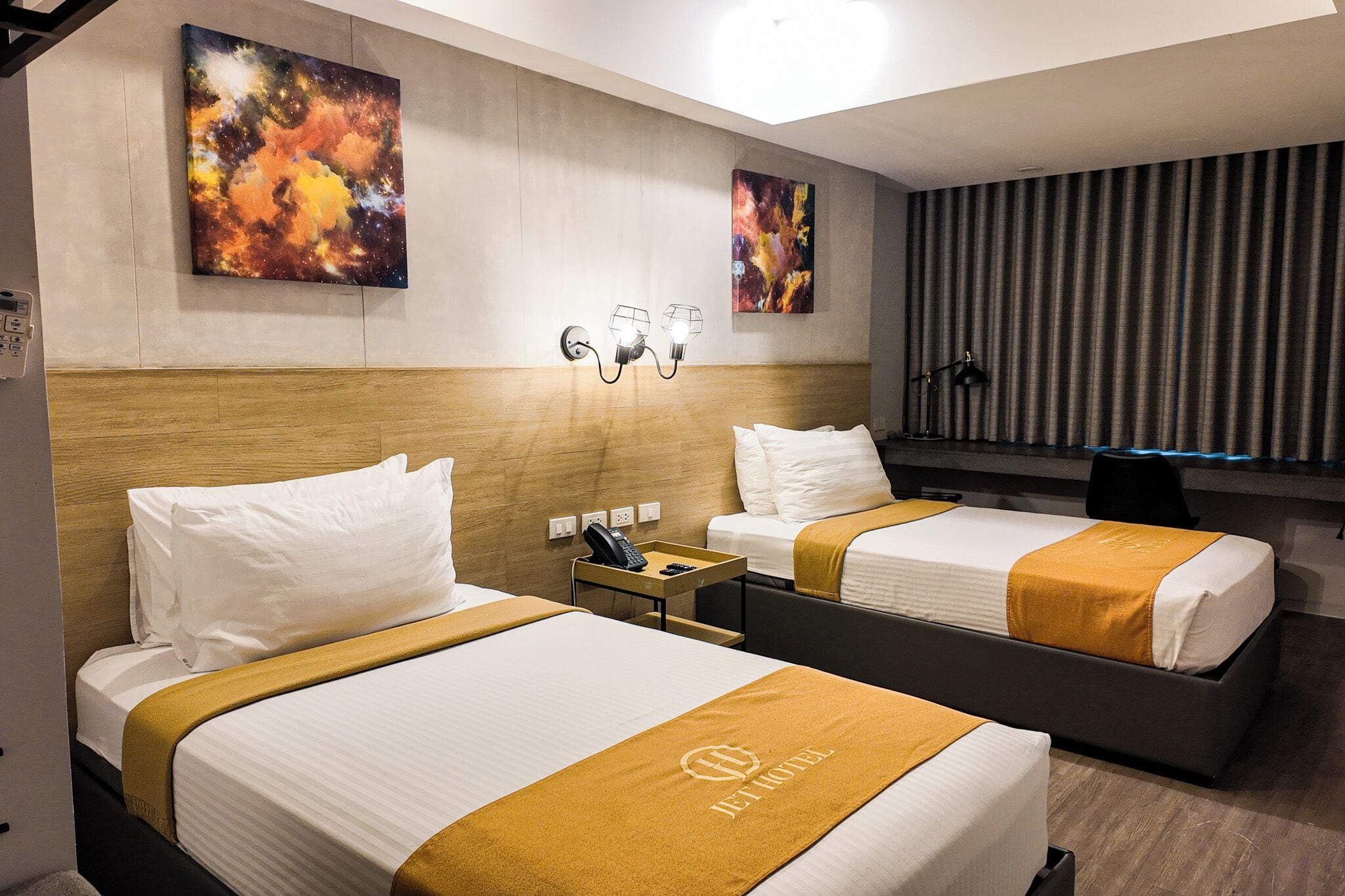 A hotel room with two beds, a nightstand, a telephone, and artwork on the walls.